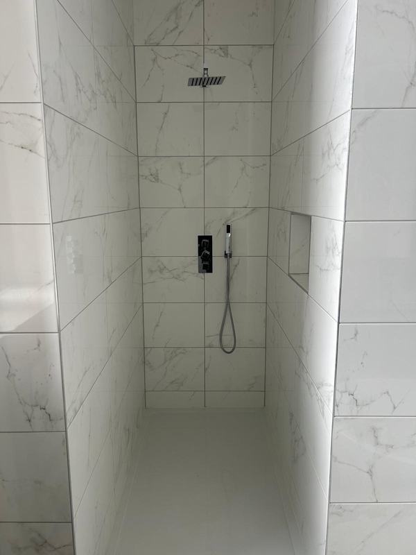 Walk-in shower tiled in marble-effect tiles with a rain head, handheld shower and recessed shelf