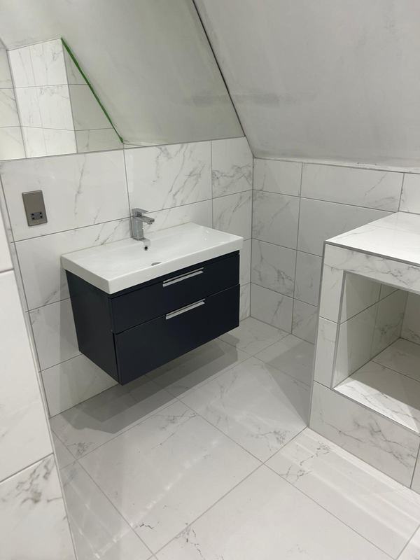 Wall-hung vanity unit with a white basin and chrome tap against marble-effect wall and floor tiles