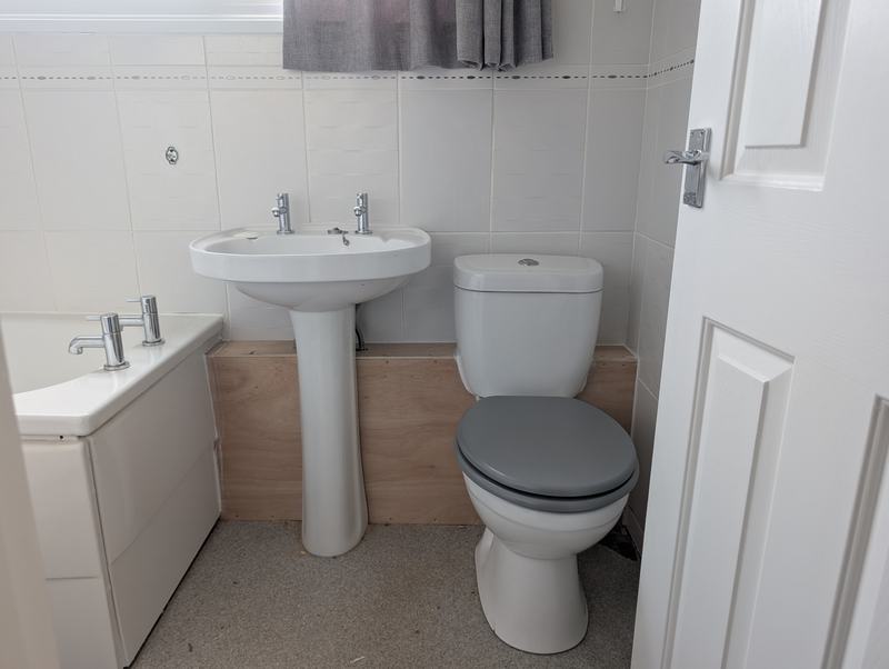 Plywood panelling boxing in the pipework behind a basin and toilet