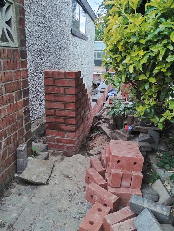 Red brick pillar and low wall being built beside a house