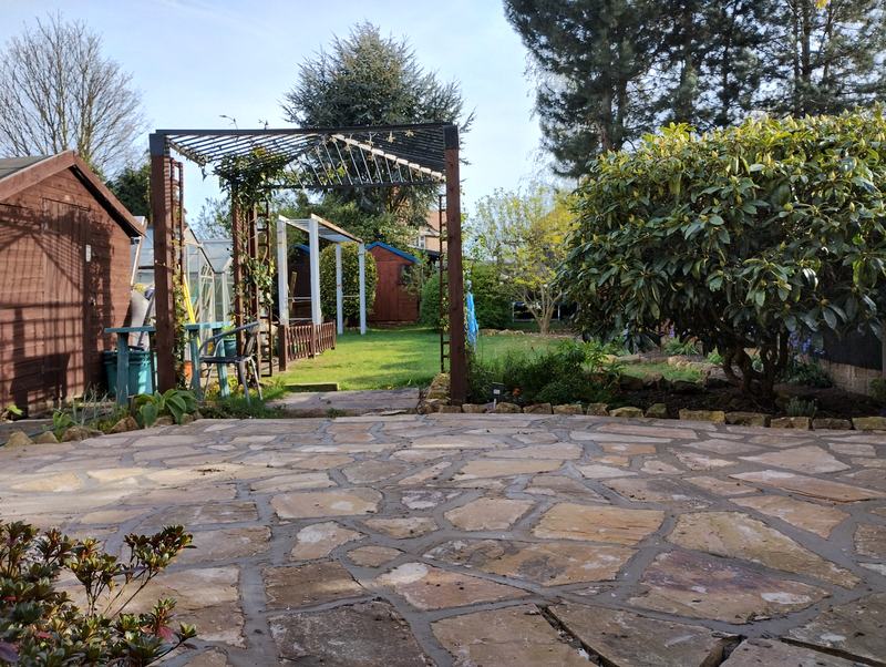 Crazy paving patio with a garden path and pergola beyond