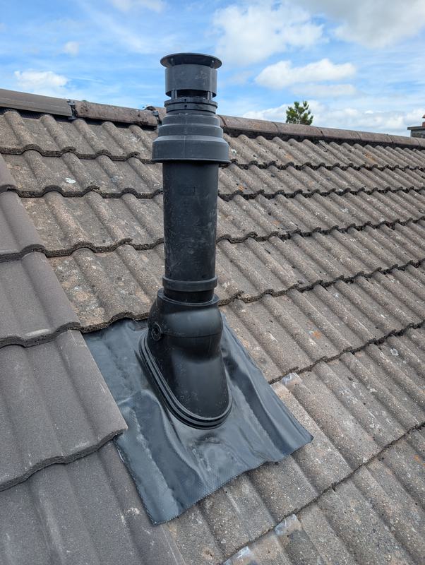 Black vertical boiler flue passing through a tiled roof with a flashing