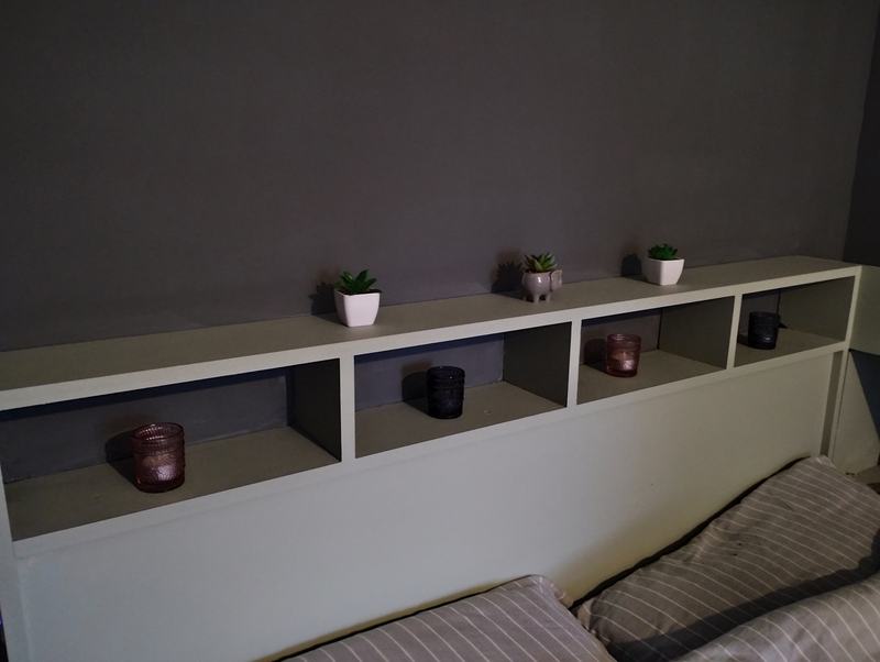 White painted headboard with four open shelves holding candles and small plants