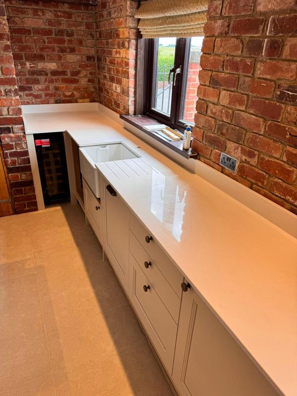 Kitchen with painted units, white worktops and a Belfast sink beside exposed brick