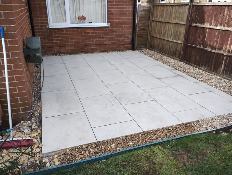 Finished paved patio edged with gravel beside a brick house