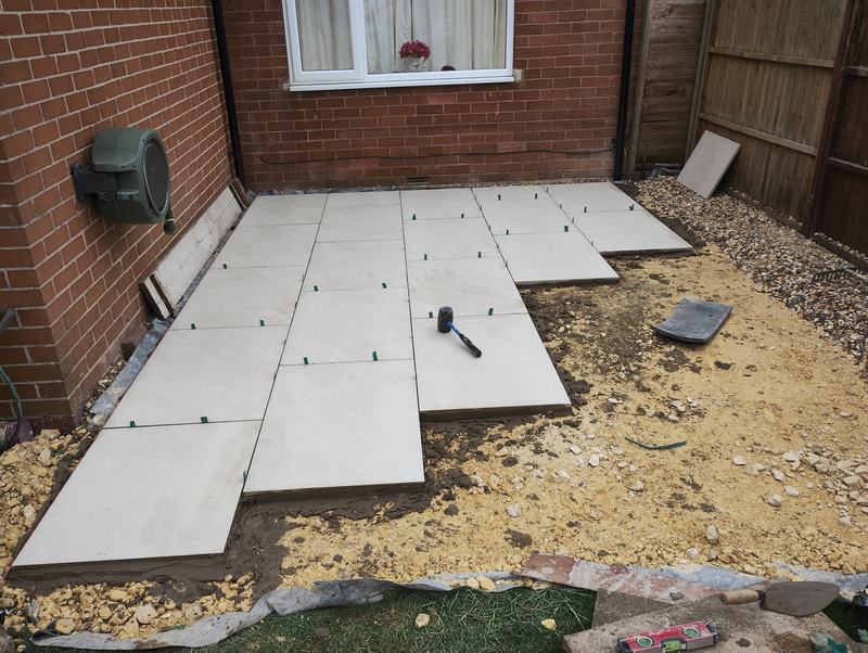 Large paving slabs being laid on a mortar bed beside a brick house