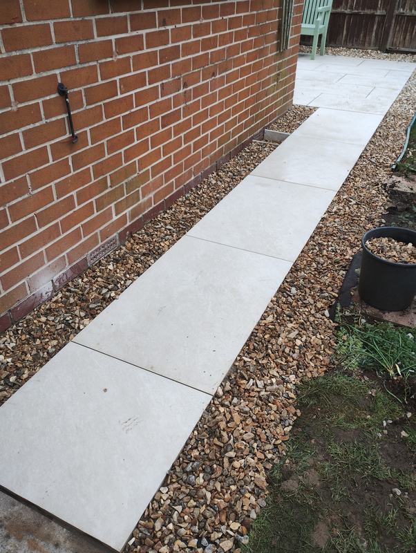 Line of large paving slabs forming a path beside a brick wall with gravel borders