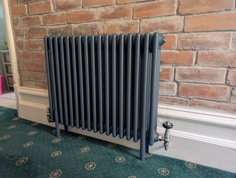 Dark grey column radiator with traditional valves against exposed brick