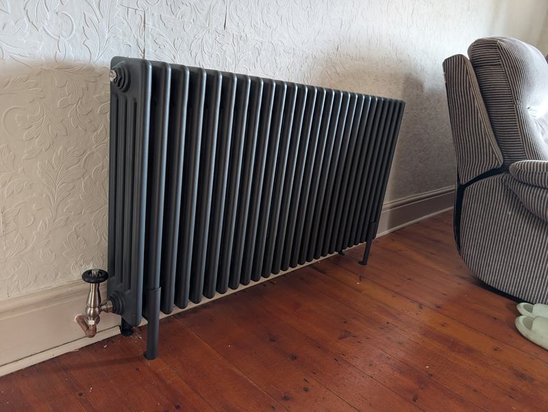 Dark grey column radiator with traditional valves on a wooden floor