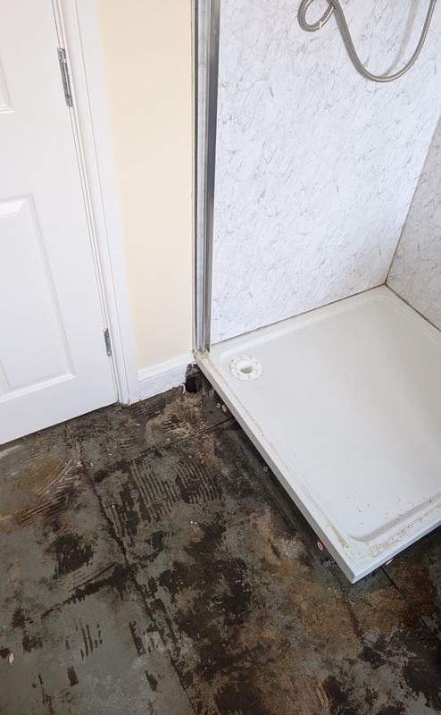 Old shower tray with a damaged, stained floor beside it