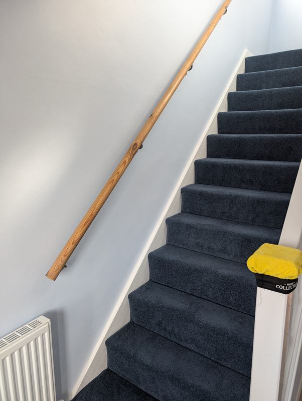 Staircase with pale blue walls, a wooden handrail and navy carpet