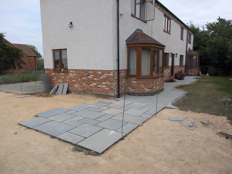 Grey stone paving path and patio being laid on sand beside a house