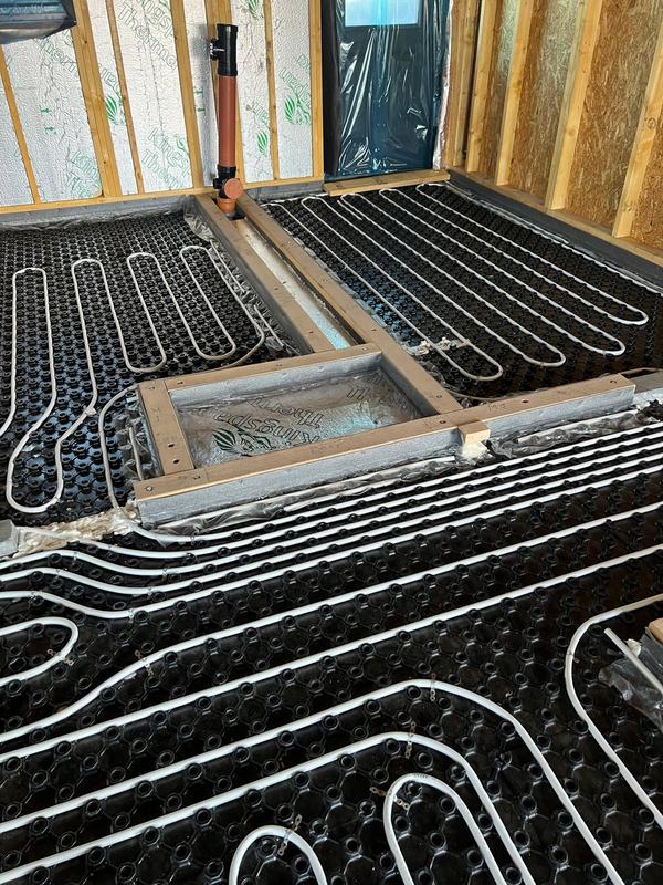 Underfloor heating pipework and a soil pipe inside a timber-frame room