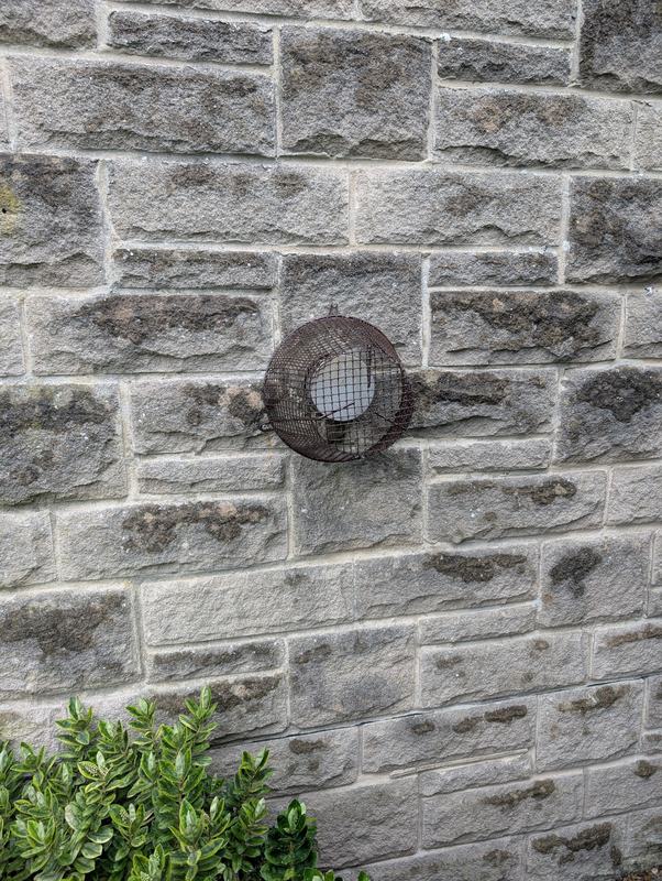 Wire mesh cover over a vent in a stone wall